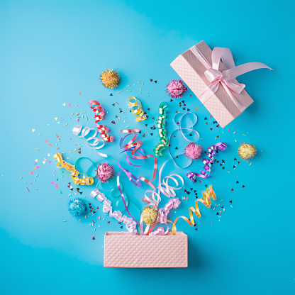 Creative layout with Christmas confetti on light blue background. Minimal birthday party or New Year celebration concept. Opened present box, surprise. Flat lay, top view, greeting card.