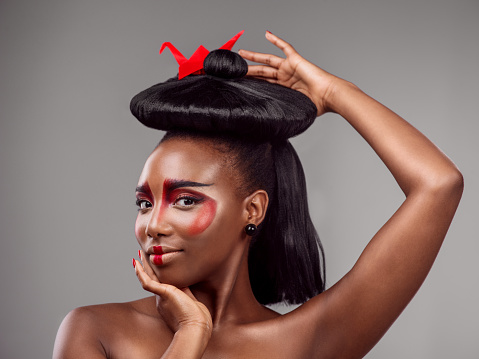 Studio shot of a beautiful young woman wearing Asian inspired makeup and posing with origami against a grey background