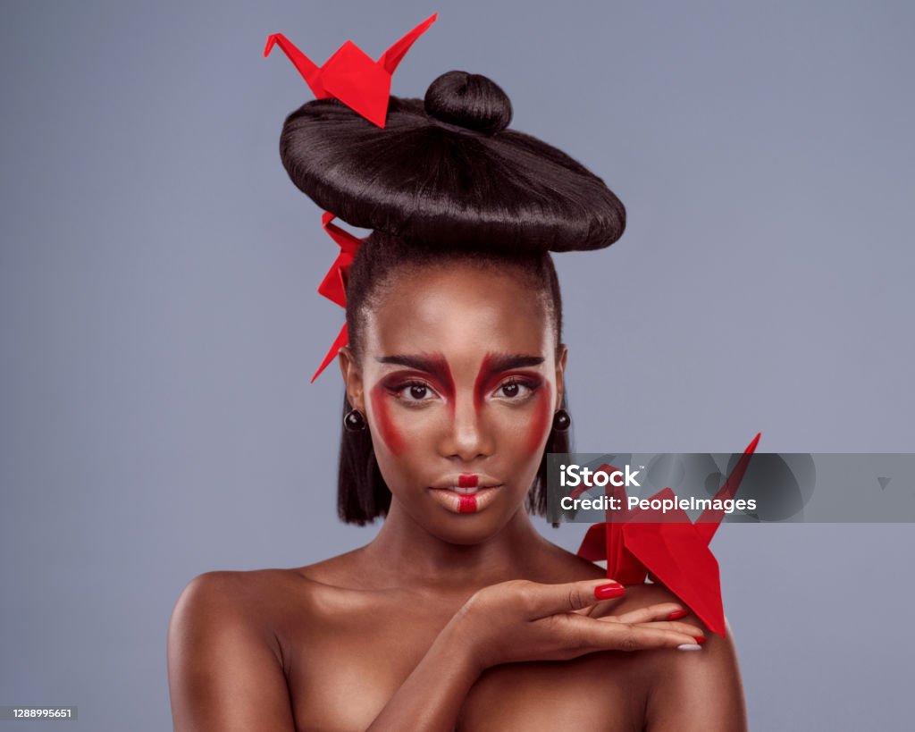 Isn’t origami just exquisite? Studio shot of a beautiful young woman wearing Asian inspired makeup and posing with origami against a grey background Haute Couture Stock Photo