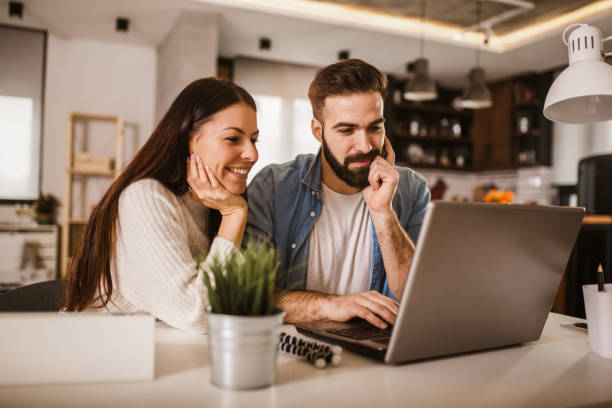 coppia felice che si gode il lavoro da casa. coppia felice che fa affari insieme lavorando a casa sul laptop. - coppia di giovani foto e immagini stock