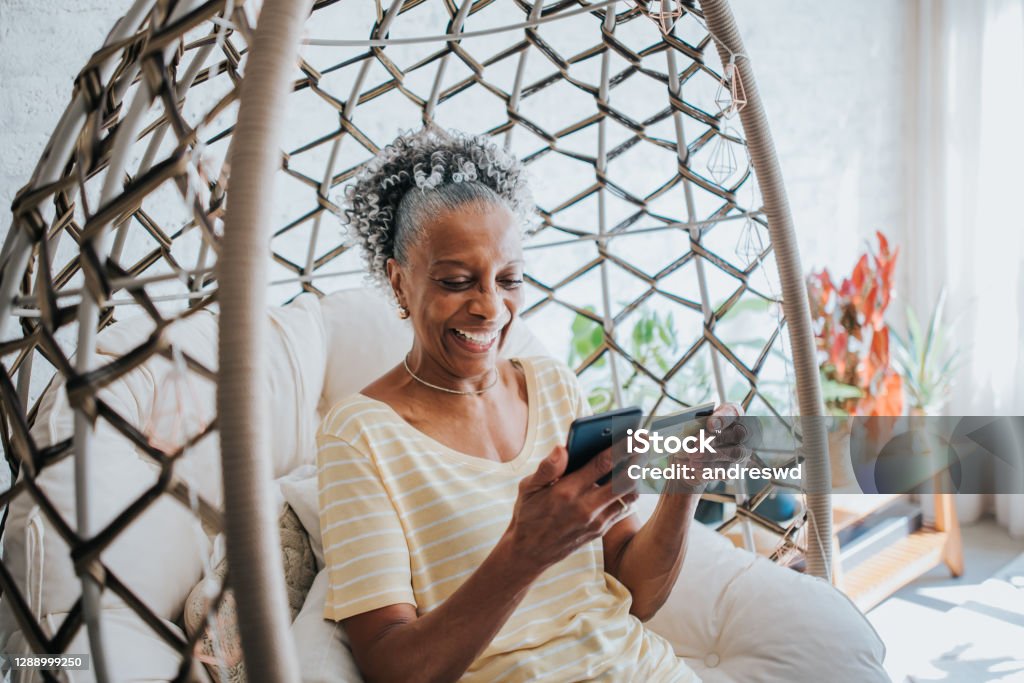 A senior woman using her credit card holding her cell phone in the living room of the house Credit Card Stock Photo