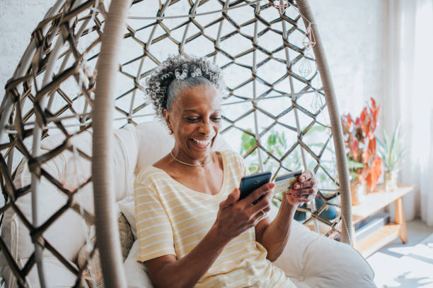 A senior woman using her credit card holding her cell phone in the living room of the house A senior woman using her credit card holding her cell phone in the living room of the house DisruptAgingCollection stock pictures, royalty-free photos & images