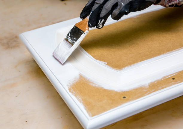 ridipingendo le porte dell'armadio della cucina con vernice di gesso bianco all'interno di casa. dare alla vecchia cucina un nuovo concetto di look. mano che tiene uno strumento pennello con vernice contro la vecchia porta dell'armadio. - armadietto da cucina foto e immagini stock