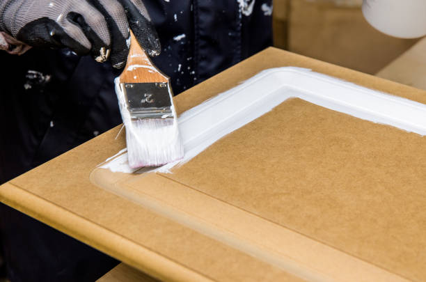 istock Repainting kitchen cabinet doors with white chalk paint indoors at home. Giving old kitchen new look concept. Hand holding a paint brush tool with paint against old cupboard door. 1289001198