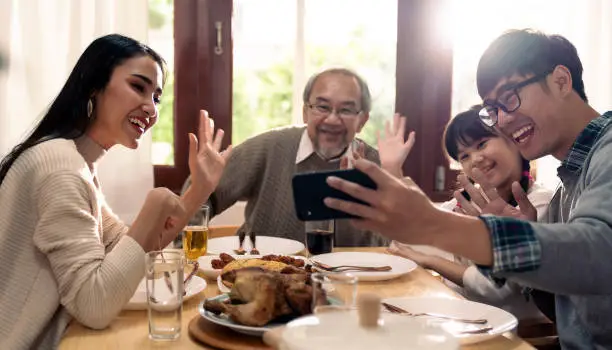 Happy asian multigenerational family of dad mom daughter girl and grandfather taking selfie together before eating lunch together at home.  Happy family engagement togetherness concept.