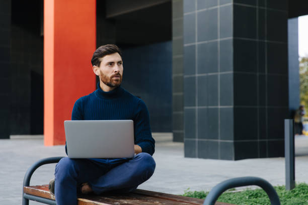 istock Thoughtful freelancer sitting in bench with laptop 1289005233