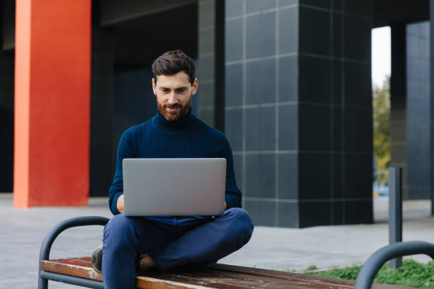 istock Bearded man browsing internet on laptop outdoors 1289005463