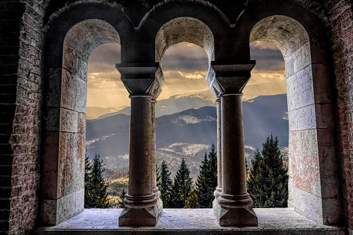 Beautiful gothic medieval arched stone window. Magnificent majestic view from the window. Winter mountains and a castle