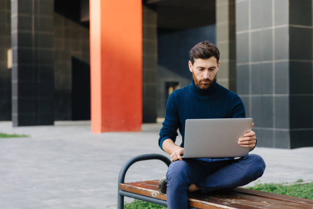 istock Handsome man sitting on bench and working on laptop 1289006612