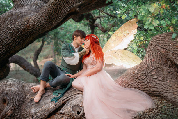 young couple in love. a man and a woman are hugging on a huge tree. themed creative wedding bright fantasy photography. fairy woman in long pink dress with bright golden wings. a man in an elf costume - long hair red hair women men imagens e fotografias de stock