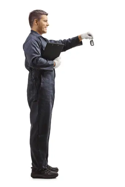 Full length profile shot of worker in a uniform giving car keys and holding a clipboard isolated on white background