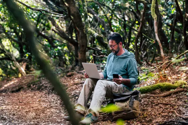 Adult young man work with online roaming connection technology outdoor with phone and laptop computer - people in nature outdoors alternative office with free job - digital nomad lifestyle