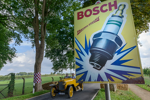 Bosch spark plug classic advertisment poster with a vintage car driving past in the background. The car is doing a demonstration drive during the 2017 Classic Days event at Schloss Dyck.