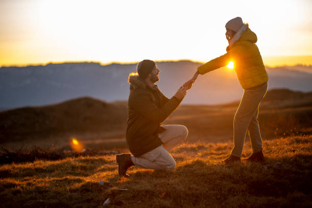She said yes! Silhouettes of a man making a marriage proposal to his girlfriend on the mountain peak at sunset. Landscape with the silhouette of lovers against the colorful sky. engagement stock pictures, royalty-free photos & images