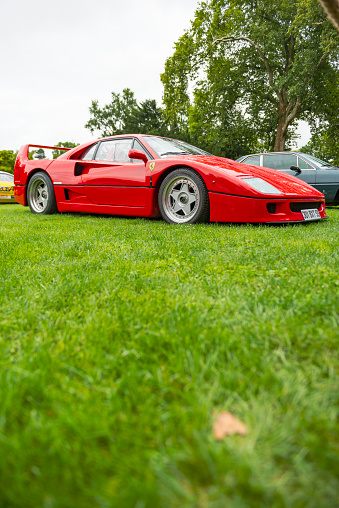 Ferrari F40 supercar of the 1980s at a classic car show. This red Ferrari is fitted with a bi-turbo V8 and was the former car of Formula 1 driver Nigel Mansell. The car is on display during the 2017 Classic Days event at Schloss Dyck. People in the background are looking at the cars.