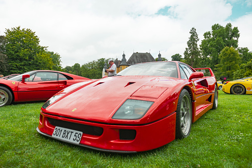 Ferrari F40 supercar of the 1980s at a classic car show. This red Ferrari is fitted with a bi-turbo V8 and was the former car of Formula 1 driver Nigel Mansell. The car is on display during the 2017 Classic Days event at Schloss Dyck. People in the background are looking at the cars.