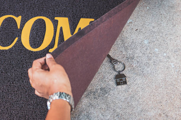 Woman revealing hidden key under doormat Woman revealing hidden key under doormat key doormat stock pictures, royalty-free photos & images