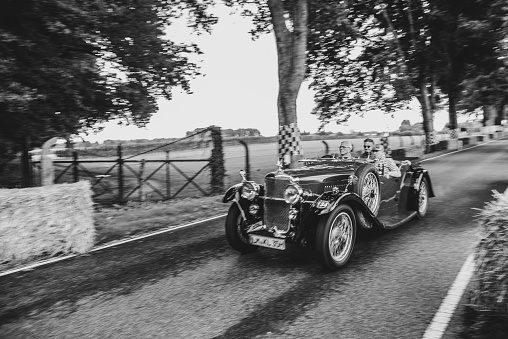 Vintage classic car driving on a country road in black and white. The car is doing a demonstration drive during the 2017 Classic Days event at Schloss Dyck.