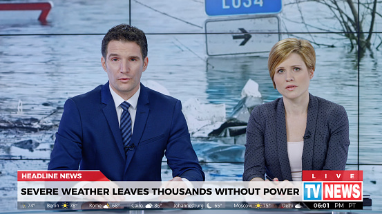 Male and female anchors presenting breaking news about extreme weather causing power outage.