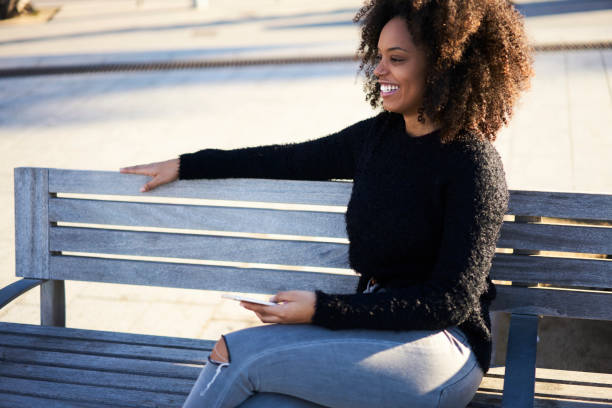 istock Smiling woman sitting on bench with smartphone 1289018372