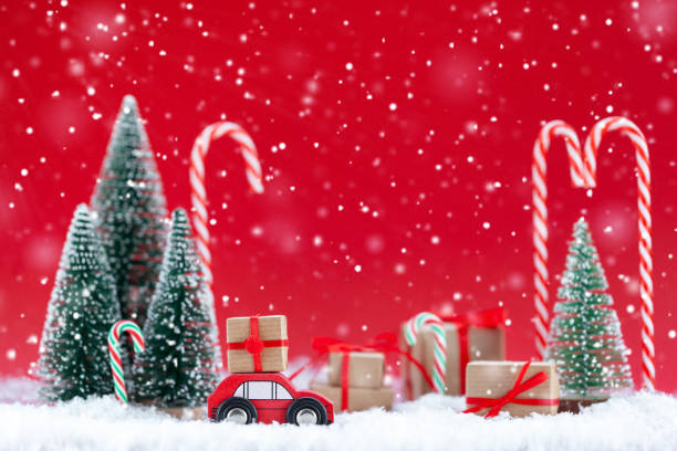 istock Festive composition Christmas red car with a gift box in a pine forest where many different presents on red background. Happy New Year card concept 1289021257