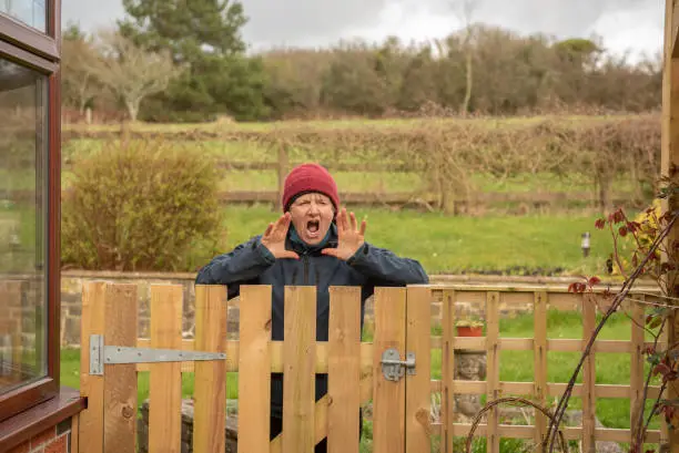 Senior woman shouting over a wooden gate outdoors in winter