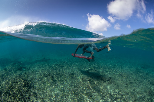 A wave breaks over a tropical reef while a local surfer dives underneath.