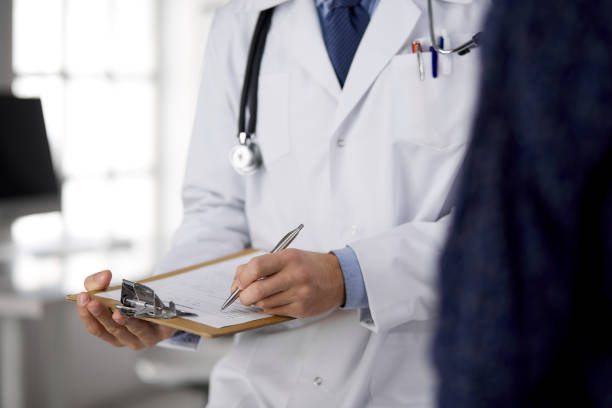 istock Unknown red-bearded doctor and patient woman discussing current health examination while sitting in sunny clinic, close-up. Medicine concept 1289023892