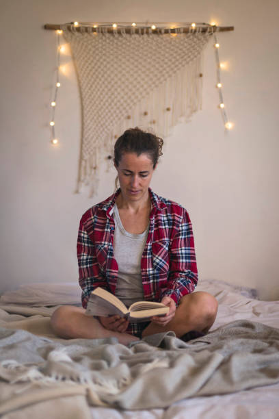 istock Woman in red shirt reading book on bed 1289026811