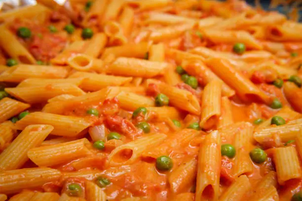 Cooking one-pot Italian penne pasta in creamy vodka tomato sauce with green peas