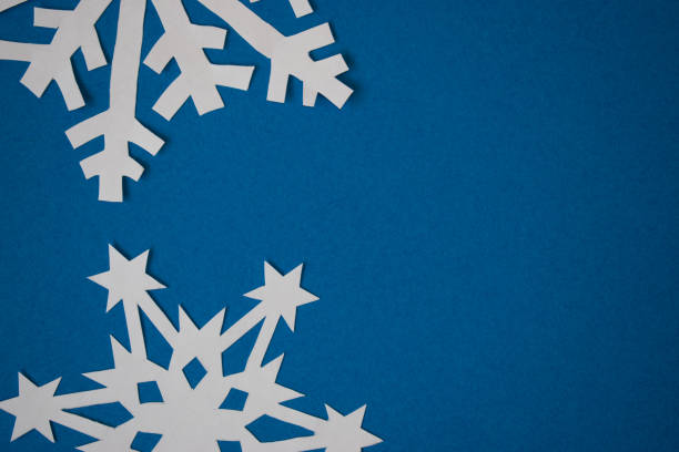 istock White cut out paper snowflakes on blue background. Greeting card 1289030018