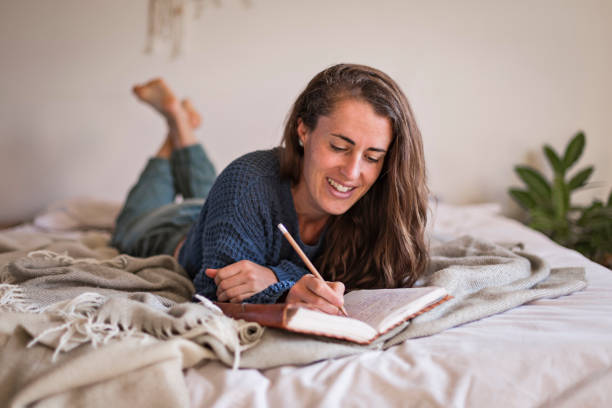 Woman lying on her bed writing in her journal Woman in blue sweater lying on her bed writing in her leatherbound journal bullet journal photos stock pictures, royalty-free photos & images