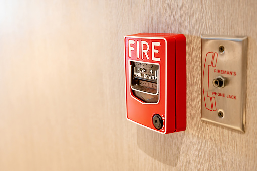 Red fire alarm switch and phone jack for fireman on wooden wall in office building. Industrial fire warning system equipment for emergency.