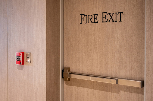 Wooden fire exit door with fire alarm and phone jack for fireman in office building. Fire evacuation and warning system equipment for emergency.