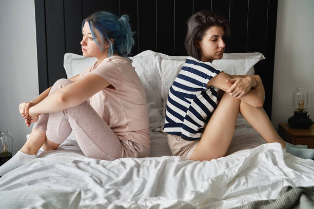 Full size photo of two attractive young women cheerful show feet dressed sleepwear outfit wake up cozy day light bedroom home interior.