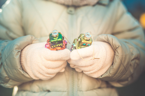 Preschool girl dressed in jacket and cap, holds in hands Christmas decorations in box. Winter 2020. Close shot. Krakow in Poland. Outdoor. 
Only one little girl
