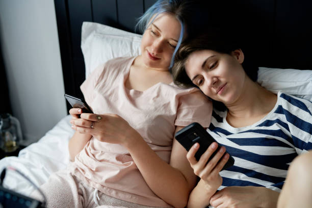 istock Romantic lesbian couple lying in bed with mobile phones 1289040129