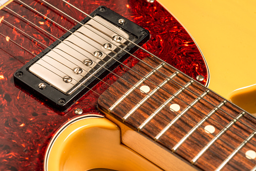 A close-up of the neck and body of an electric guitar, with a chrome-plated humbucker pickup below the strings.