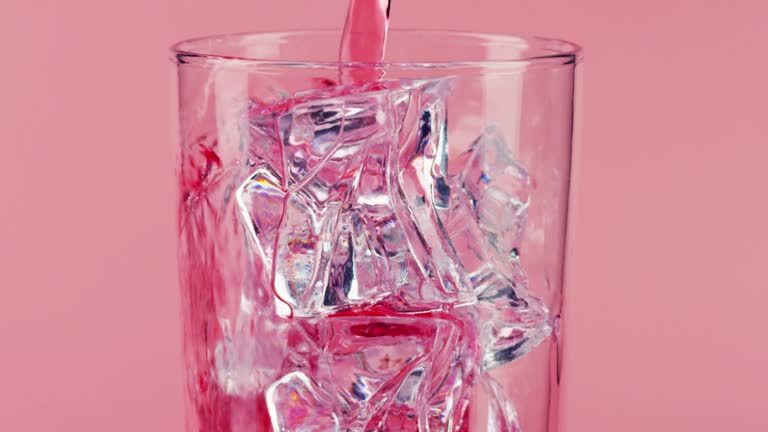 Pouring pink drink into a glass with ice on pink background, close-up slow motion shot on Red