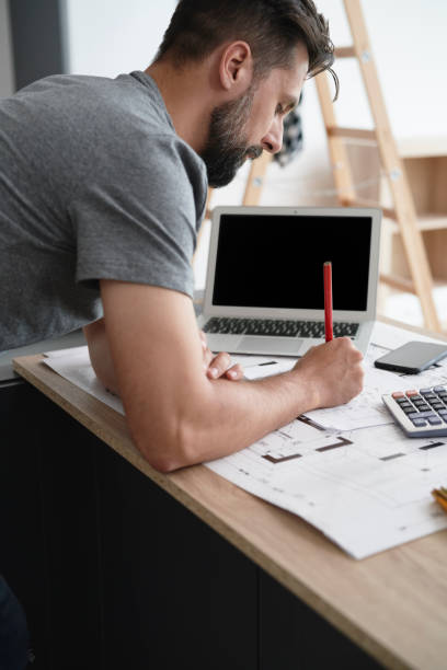 istock Carpenter in front of a computer making corrections to plans 1289047742