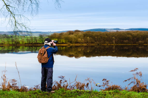 istock Senior grey haired man using his mobile phone to photograph a still Scottish loch on an autumn morning 1289050799