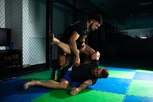 BJJ Fighters are practicing Brazilian jiu-jitsu techniques in a dark gym