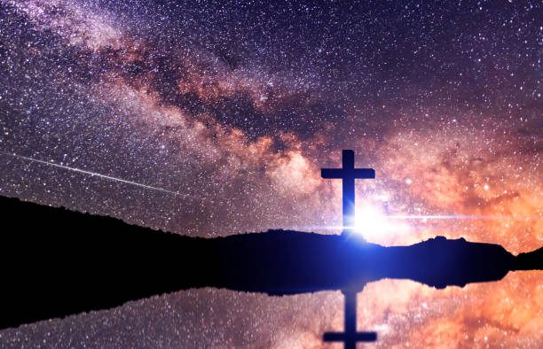 The cross silhouette on on the hill in night , behinde bright milky way galaxy and light rays. stock photo