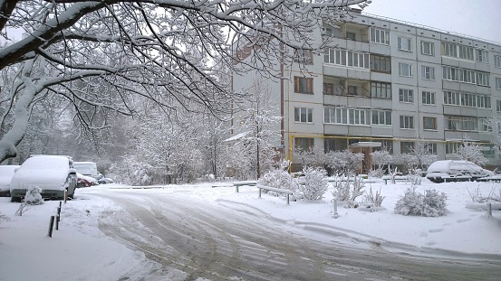Winter is here. Snowfall in the city. White snow covered tree, cars and road near apartment residential building. Chilly. Cityscape. Nobody. Beauty in nature. Problem of street Snow removal. Frosty