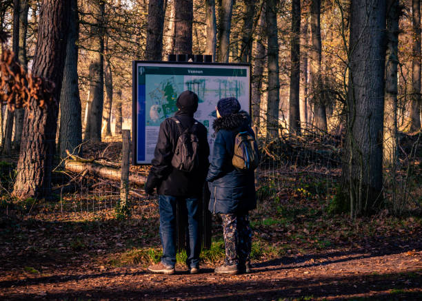 two people looking at a information board Borger, The Netherlands November 25th: Two people with small backpacks, wearing thick winter coats and warm woolen hats looking at the information board of a national park. fen photos stock pictures, royalty-free photos & images