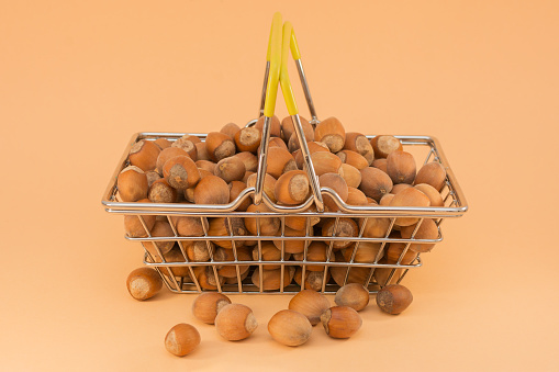 a huge amount of hazelnuts are in the shopping basket, some are nearby. Horizontal photo, close-up, beige background. The idea is to wholesale any goods