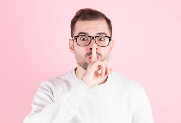 istock Young handsome man over pink background asking to be quiet with finger on lips. Silence and secret concept. 1289058991