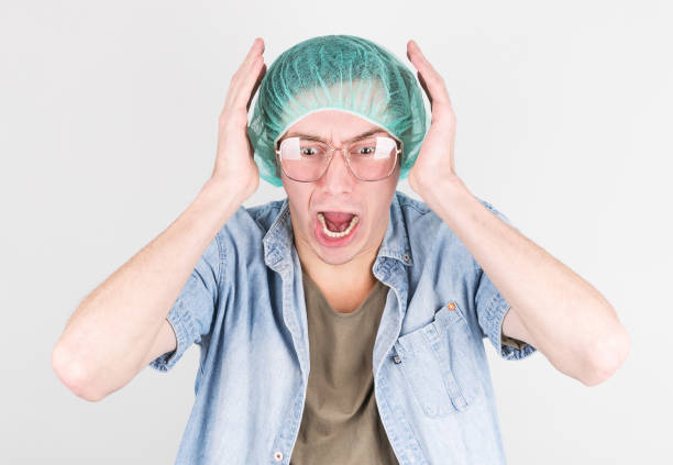 a young man in a medical cap and glasses screams in fright during childbirth on a gray background. concept of childbirth process. - labour room imagens e fotografias de stock