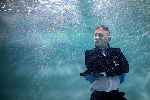 Young businessman folded his hands and strictly looks towards underwater. Emotional person is Director in pond. Concept of working hours and making business decisions in office. Copy space