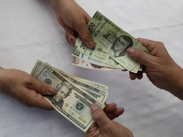hands exchanging Mexican pesos and American dollar money